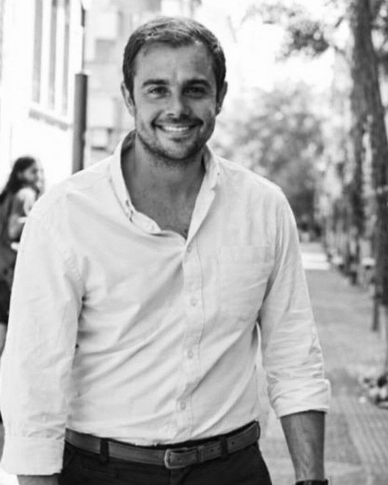 Retrato de Nacho Medina, sonriendo, con camisa clara, en una calle